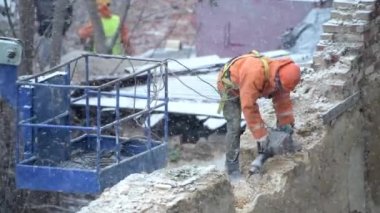 Terk edilmiş eski evin yıkılması, turuncu kasklı işçinin kar yağdığında duvarı matkapla delmesi. Oturma odasının yeniden inşası. Kentsel Yenilenme 4k Yüksek kalite video