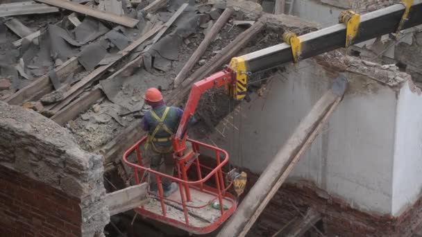 Знесення старого покинутого будинку, робітника в помаранчевому шоломі в кошику крана знищують дерев'яний дах бензопилою. Деконструкція житлового будинку. Міське оновлення 4k Високоякісне відео — стокове відео