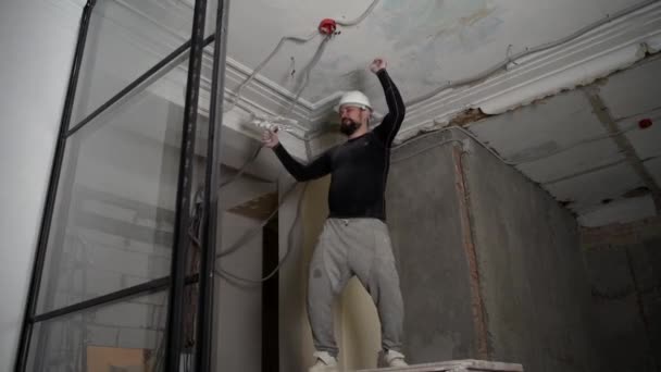 Tlustý vousatý dospělý muž v ochranné přilbě a černě přiléhavé oblečení odstranit konstrukce běloba vintage vysoký strop. Opravu opravte vlastníma rukama. Záznam zpomalení 4k — Stock video