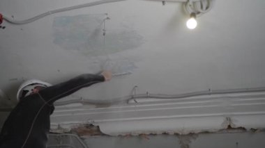 Koruyucu kasklı ve siyah dar elbiseli şişman sakallı yetişkin adam inşaat beyazlatıcısının yüksek tavanını kaldırıyor. Tamiratı kendi el konseptinle yap. 4k ağır çekim görüntüleri 