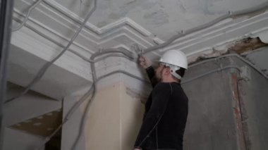 Koruyucu kasklı ve siyah dar elbiseli şişman sakallı yetişkin adam inşaat beyazlatıcısının yüksek tavanını kaldırıyor. Tamiratı kendi el konseptinle yap. 4k ağır çekim görüntüleri 