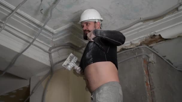 Fat bearded adult man in protective helmet and black tight fitting clothing remove construction whitewash vintage high ceiling. Overhaul repair with your own hands concept. 4k slow motion footage — Stock Video