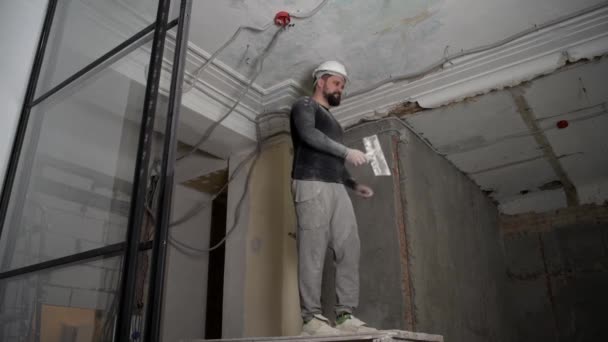 Fat bearded adult man in protective helmet and black tight fitting clothing remove construction whitewash vintage high ceiling. Overhaul repair with your own hands concept. 4k slow motion footage — Stock Video