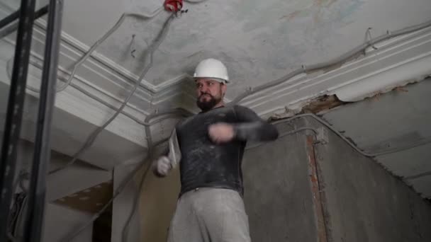 Tlustý vousatý dospělý muž v ochranné přilbě a černě přiléhavé oblečení odstranit konstrukce běloba vintage vysoký strop. Opravu opravte vlastníma rukama. Záznam zpomalení 4k — Stock video