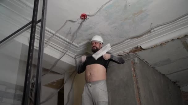 Vet bebaarde volwassen man in beschermende helm en zwart strak passende kleding verwijderen constructie whitewash vintage hoog plafond. Revisie reparatie met uw eigen handen concept. 4k slow motion beelden — Stockvideo