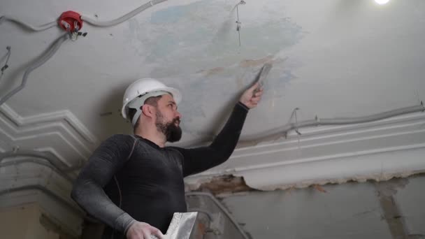 Fat bearded adult man in protective helmet and black tight fitting clothing remove construction whitewash vintage high ceiling. Overhaul repair with your own hands concept. 4k slow motion footage — Stock Video