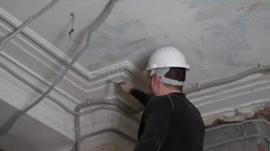 Koruyucu kasklı ve siyah dar elbiseli şişman sakallı yetişkin adam inşaat beyazlatıcısının yüksek tavanını kaldırıyor. Tamiratı kendi el konseptinle yap. 4k ağır çekim görüntüleri 