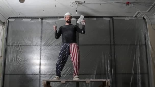 Fat bearded adult man in protective helmet and USA flag print on pants remove construction whitewash vintage high ceiling. Overhaul repair with your own hands concept. 4k slow motion footage — Stock Video