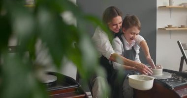 Mutlu genç kadın ve şirin çocuk atölyede dönen çömlek çarkında toprak malzemesi yapıyorlar. Yavaş çekim