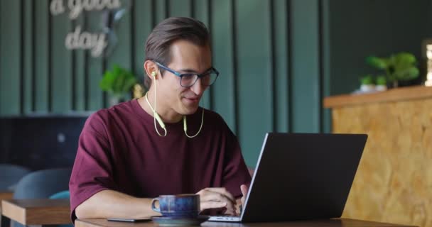 Молодий чоловік робить відеодзвінок через ноутбук, сидячи в кав'ярні — стокове відео