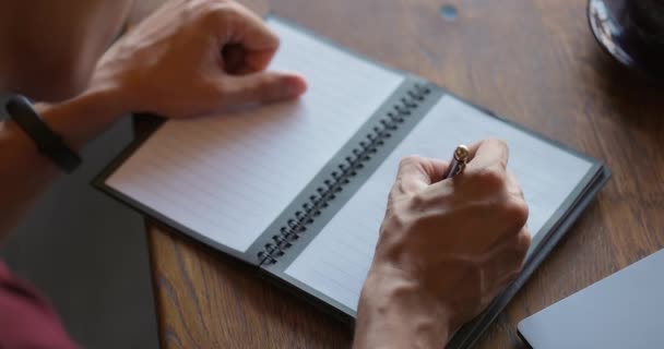 Escribir con bolígrafo en un cuaderno y luego cerrarlo. Vista de cerca de las manos con bloc de notas en la mesa de madera, vista superior. Movimiento lento — Vídeo de stock