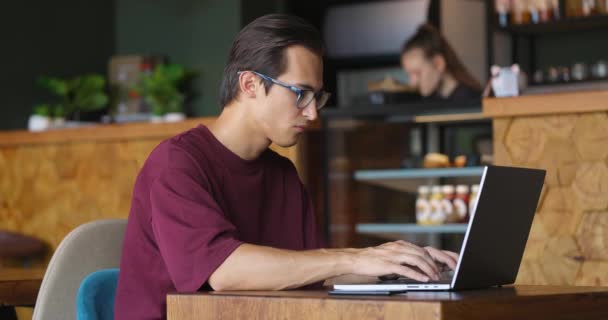 Πλάγια εικόνα ελεύθερου επαγγελματία πληκτρολογώντας σε πληκτρολόγιο laptop στο cafe — Αρχείο Βίντεο