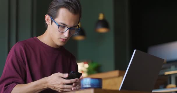 Σοβαρός νεαρός επιχειρηματίας που χρησιμοποιεί το τηλέφωνο σε καφετέρια ελέγχοντας τα μηνύματα. — Αρχείο Βίντεο