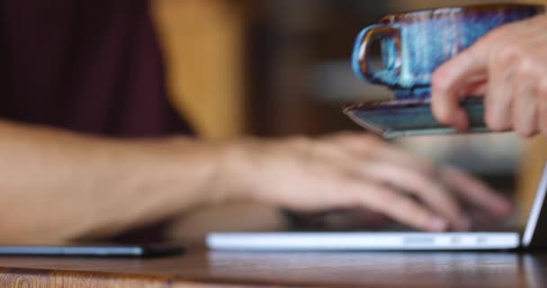 Vista lateral del hombre escribiendo en el ordenador gris mientras toma un descanso de café en la acogedora cafetería — Vídeo de stock