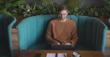 Gündüz kafede oturan ve uzaktan kumanda için dizüstü bilgisayarı kullanan adamın en iyi görüntüsü. Tabutta çalışan, gözlüklü, yakışıklı, serbest çalışan bir iş adamı. Öğrenciler çevrimiçi çalışıyor