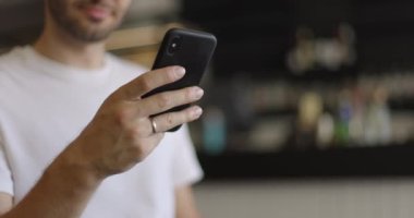 Kahve dükkanında akıllı telefon kullanan erkek eli yakın çekim. Mesajlaşmak, çalışmak, günlük video izlemek, iletişim kurmak. Yavaş çekim