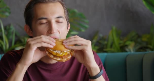 Close up of young handsome brunet eating burger in nice coffee shop.Man enjoying meal — Stock Video