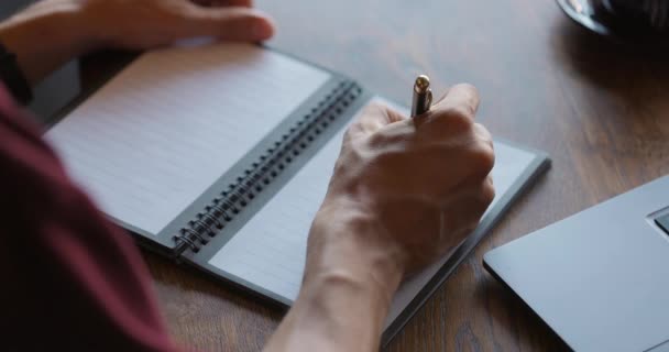 Unknown man writing notes in his paper notebook with ballpen.Guy working remotely with laptop — Stock Video