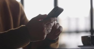 Dizüstü bilgisayar başında çalışırken cep telefonu kullanan saatli bir adamın yan görüntüsü. Erkek parmaklar akıllı telefondan yazıp dinliyorlar. Mesaj ve kaydırma. Yavaş çekim.