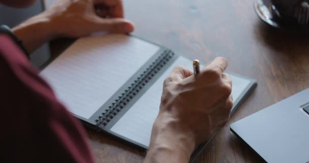 Mans Hände machen wichtige Notizen in Papiertagebuch mit Pen.Guy in rotem T-Shirt arbeitet am Holztisch — Stockvideo