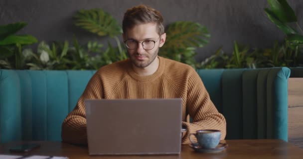 Vista frontal del hombre guapo en gafas en suéter marrón acabados trabajar en el ordenador portátil, cerrarlo y mirar hacia otro lado. Pensando en la solución de problemas de búsqueda de inspiración. Movimiento lento — Vídeos de Stock