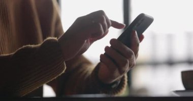 Dizüstü bilgisayar başında çalışırken cep telefonu kullanarak saatli erkek ellerini yakın plan çek. Erkek parmaklar akıllı telefondan yazıp dinliyorlar. Mesaj ve kaydırma. Yavaş çekim.