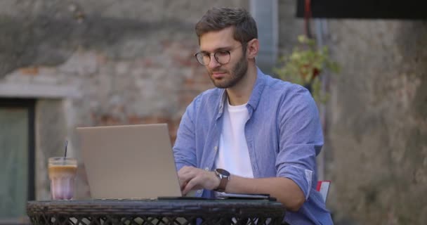 Los hombres que trabajan en el ordenador portátil y beber café helado en la cafetería al aire libre. Educación a distancia, e-learning. Movimiento lento. — Vídeos de Stock