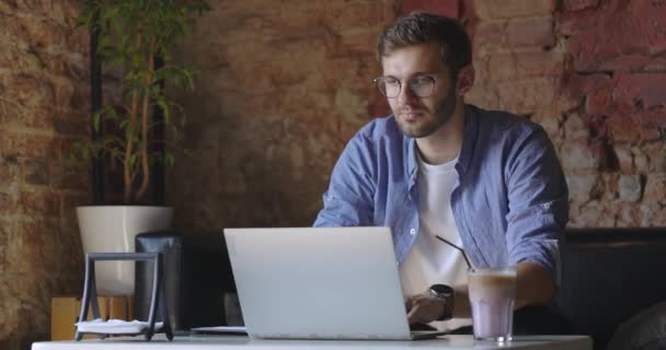 Продуманий серйозний чоловік в окулярах сидить з ноутбуком, думаючи про рішення в кафе. Повільний рух — стокове відео