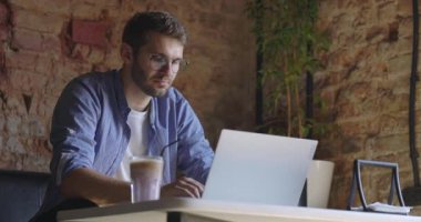 Gözlüklü düşünceli ciddi bir adamın orta görüşü laptopuyla oturup kafede çözüm düşünmesi. Yavaş çekim