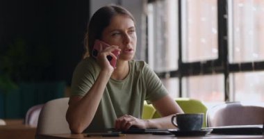 Kafede masabaşında çalışırken cep telefonuyla konuşan esmer saçlı çekici bir kadının portresi.