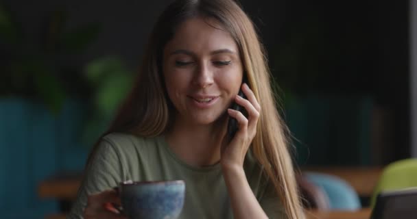 Sonriente joven mujer de negocios profesional hablando por teléfono sentarse en el escritorio de la cafetería, cliente femenina feliz hacer llamada móvil que confirma las compras en línea. Termina la llamada, cámara lenta — Vídeos de Stock