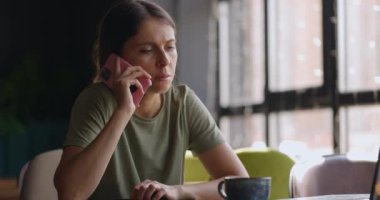 Kafede masabaşında çalışırken cep telefonuyla konuşan esmer saçlı çekici bir kadının portresi.