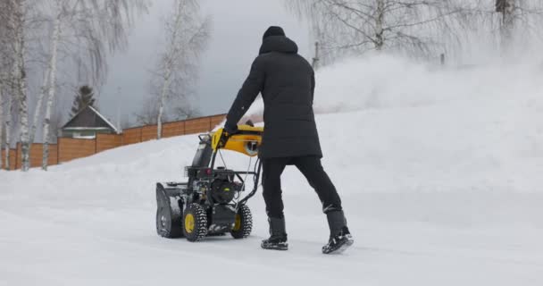 Un homme nettoie la neige avec une souffleuse à neige dans la cour à la chute de neige au ralenti — Video