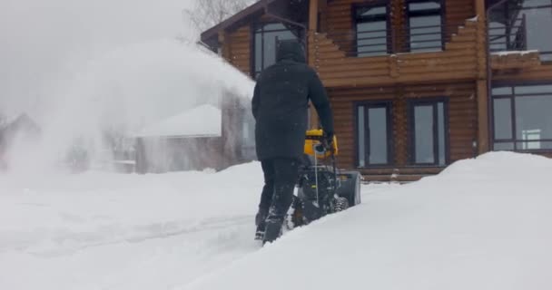 Människan tar bort snö med snöslunga på gården vid snöfall i slow motion. Bakifrån — Stockvideo