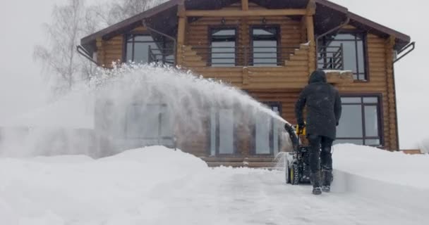 Man removes snow with snowblower in yard at snowfall in slow motion. Back view — Stock Video