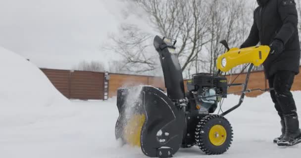 El hombre limpia la nieve con nieve Plow fondo de la casa de madera después de fuertes nevadas. Vista frontal. Movimiento lento — Vídeos de Stock