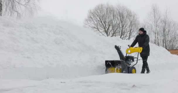 Een man die met een sneeuwblazer werkt. Sneeuwwitje winter. De mens verwijdert sneeuwvlokken met sneeuwploeg. Zijaanzicht. Koud weer. Langzame beweging — Stockvideo