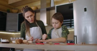 Genç anne ve oğlu mutfakta birlikte kurabiye pişiriyorlar. Anne ve bebek şekilli ev yapımı kurabiyeleri kestiler. Yan görüş. Yavaş çekim