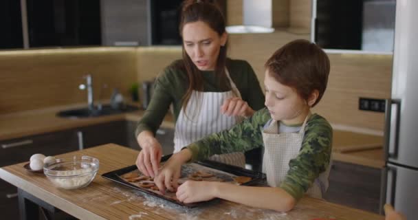 Ευτυχισμένη μητέρα και ο μικρός της γιος άπλωσαν μπισκότα σε ένα ταψί. Μαγειρεύοντας μπισκότα μαζί στην κουζίνα. Οικογενειακή μέρα, μαγειρική, ιδέα μαμάς και γιου. Αργή κίνηση — Αρχείο Βίντεο