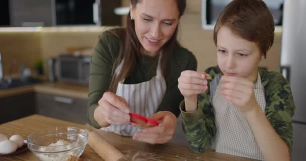 Junge Mutter und Sohn backen gemeinsam in der Küche Plätzchen. Mutter und Kind schneiden selbstgebackene Plätzchen mit Formen aus. Zeitlupe — Stockvideo