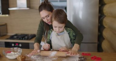 Anne ve küçük oğlu evde el yapımı kurabiyeler yapıyor, mutfakta çiğ hamuru birlikte yuvarlıyorlar. Anne babasıyla yemek pişiren çocuk. Ön manzara. Yavaş çekim