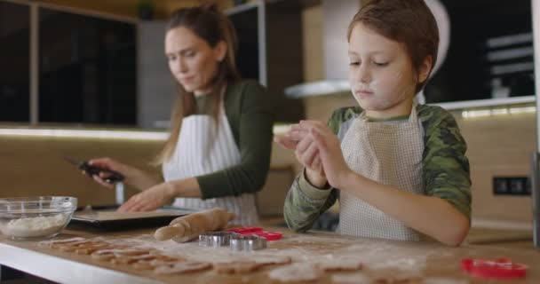Ung familj mor och son gör hembakade kakor vid köksbordet arbetar med deg leende prata. Hälsosam mat, livsstil och föräldraskap koncept. Långsamma rörelser — Stockvideo