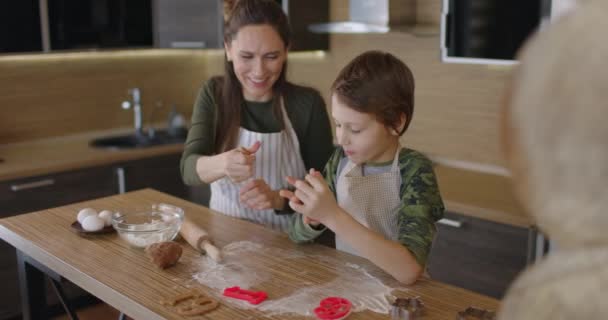 Młoda rodzina matka i syn pieką domowe ciasteczka przy kuchennym stole, pracując z ciastem, uśmiechając się. Zdrowe jedzenie, styl życia i pojęcie rodzicielstwa. Zwolniony ruch — Wideo stockowe