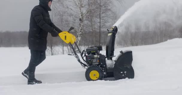 Mannen rengör snö med snö Plow bakgrund av trä hus efter tung snö. Snöplog på jobbet. Långsamma rörelser — Stockvideo
