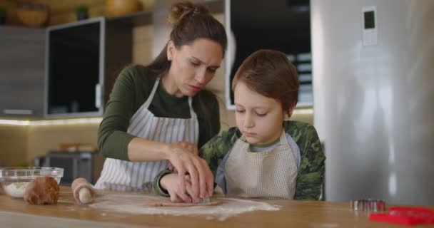 Młoda rodzina matka i syn pieką domowe ciasteczka przy kuchennym stole, pracując z ciastem, uśmiechając się. Zdrowe jedzenie, styl życia i pojęcie rodzicielstwa. Zwolniony ruch — Wideo stockowe