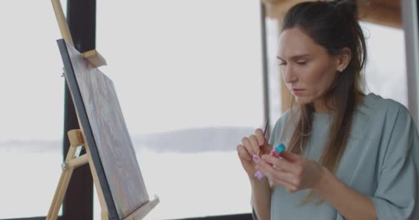 Jonge mooie vrouw is tekening in de slaapkamer, zittend op stoel in de buurt van ezel met doek, vrouwelijke kunstenaar werkt — Stockvideo
