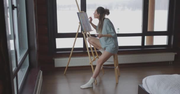 Fiatal csinos nő rajz kép a hálószobában, ül a széken közel állvány vászonnal, női művész dolgozik — Stock videók