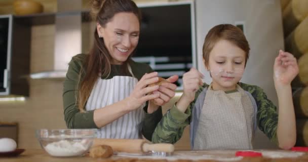 젊은 가족 엄마와 아들 이 부엌에서 손수 만든 쿠키를 만들고 있습니다. 어머니는 아들들의 얼굴에서 밀가루를 닦아 낸다. 건강에 좋은 식품, 생활 방식 및 부모로서의 개념. — 비디오