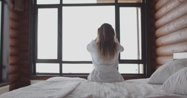 Vue arrière de la femme se réveillant et étirant la main sur le lit à la maison en bois. Mouvement lent — Video