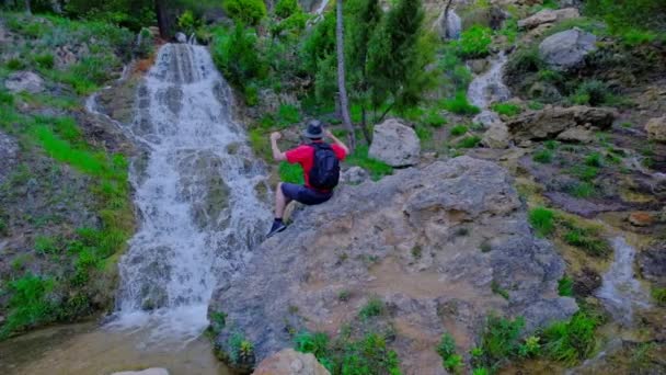 Man is sitting on a stone and raising his hands up. — Video